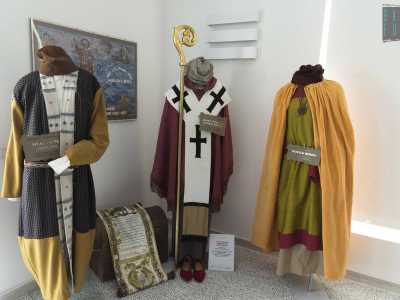 Alla sua sinistra spicca il look caratteristico dei nobili russi, costituito da un lungo mantello arancione che sottende una tunica verde oliva e a tratti rossa. Sulla destra ci sono due indumenti peculiari dei mercanti armeni: un camicione bianco dai motivi geometrici mediorientali con sopra una veste blu a maniche dorate